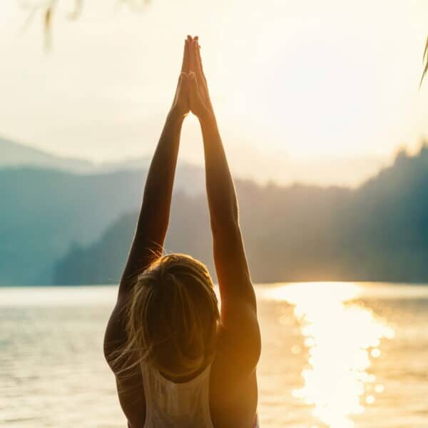 Beautiful woman practicing Yoga by the lake - Sun salutation series - Upward hands pose - Toned image